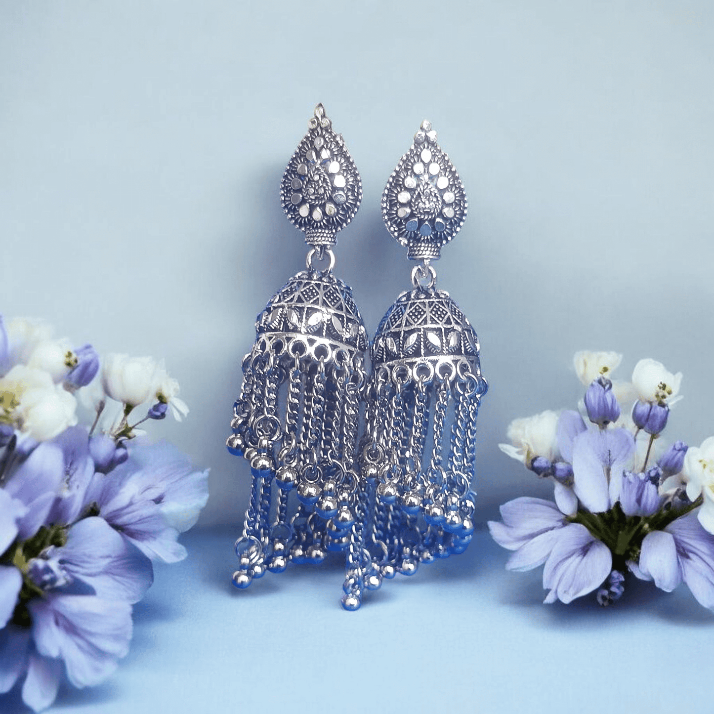 "Oxidized silver jhumka earrings with dome design and chain tassels on a Floral background – traditional Indian ethnic jewelry"