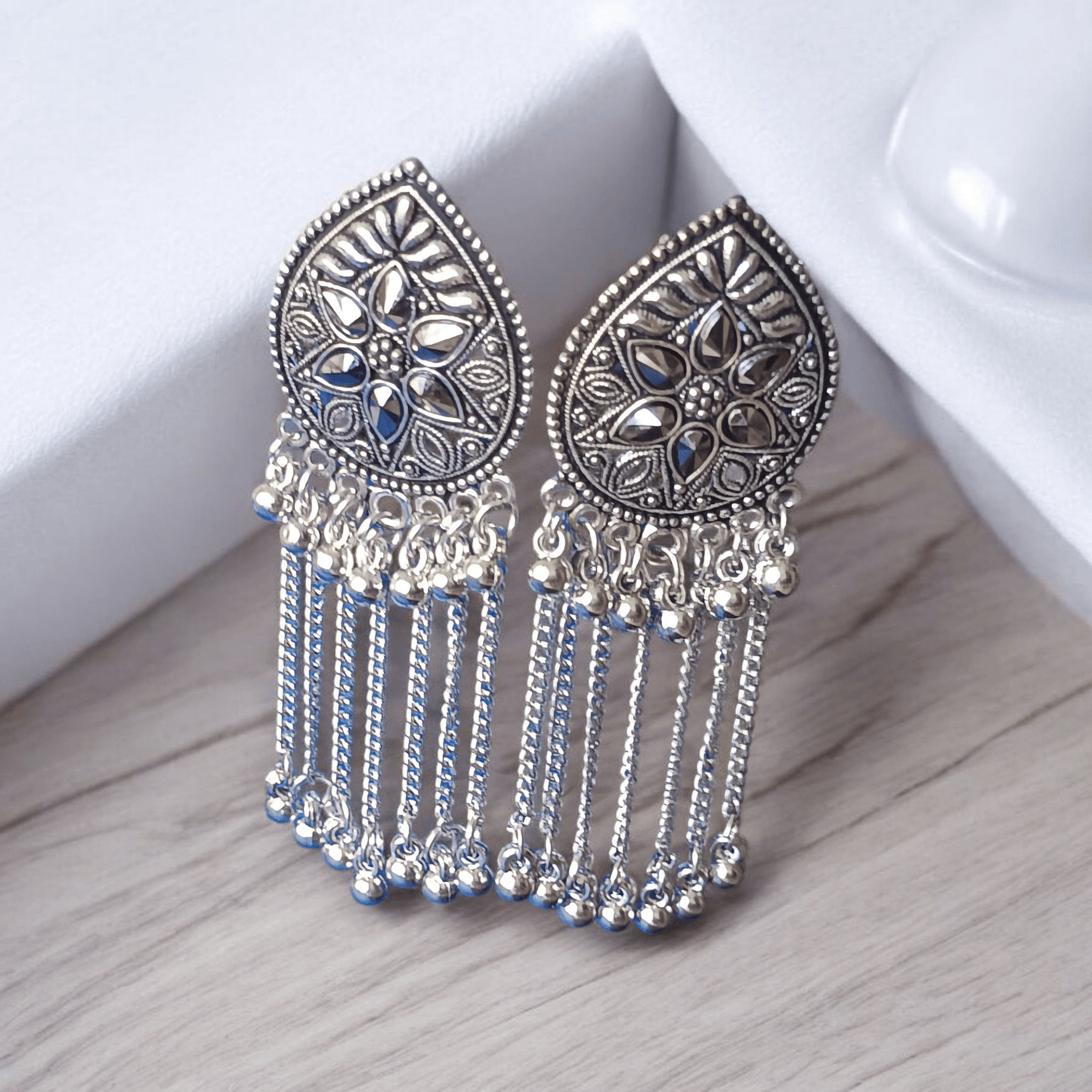 "Oxidized silver floral earrings with chain dangles on wooden background surrounded by fabric