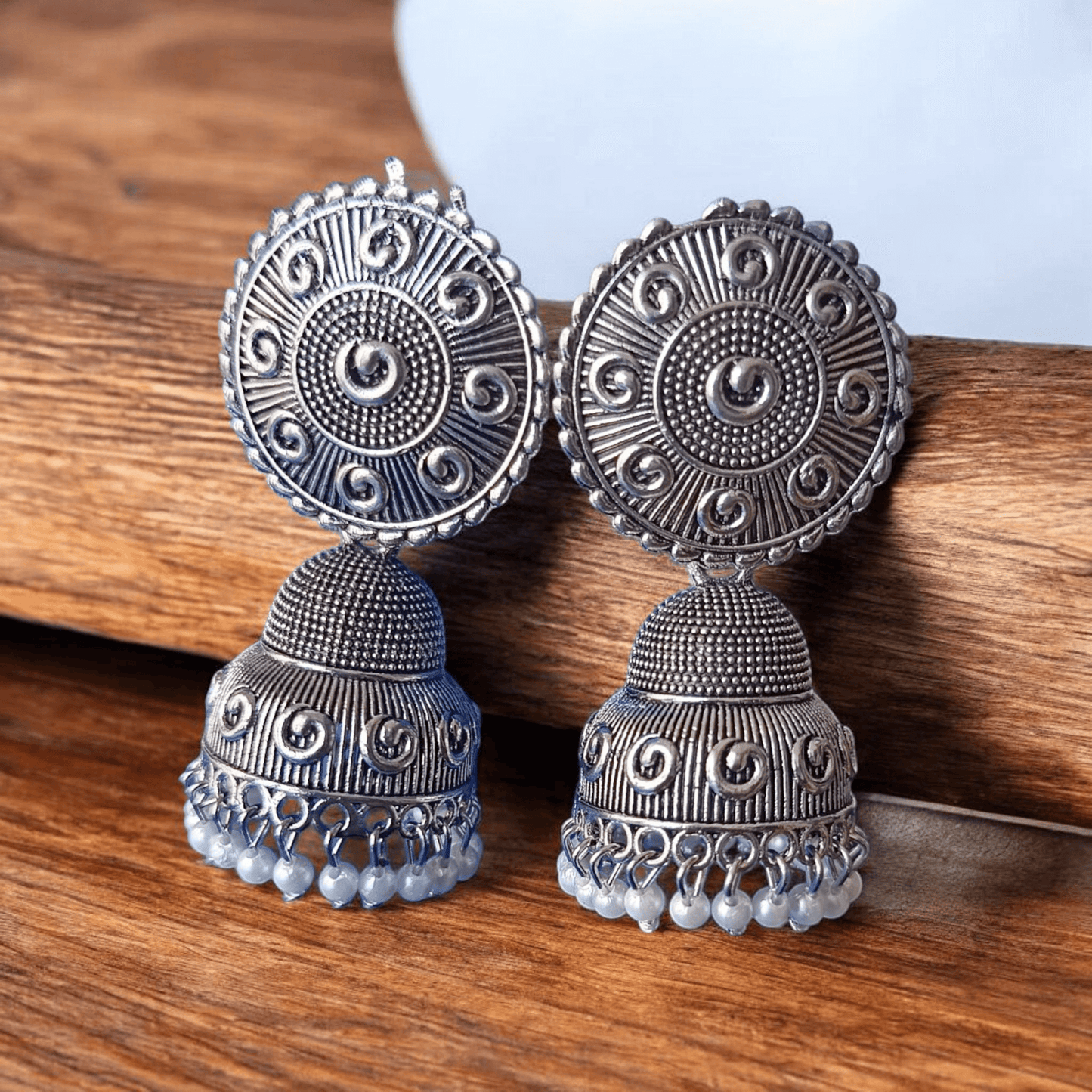 Handcrafted oxidized silver jhumka earrings with intricate designs and pearl drops against a wooden background