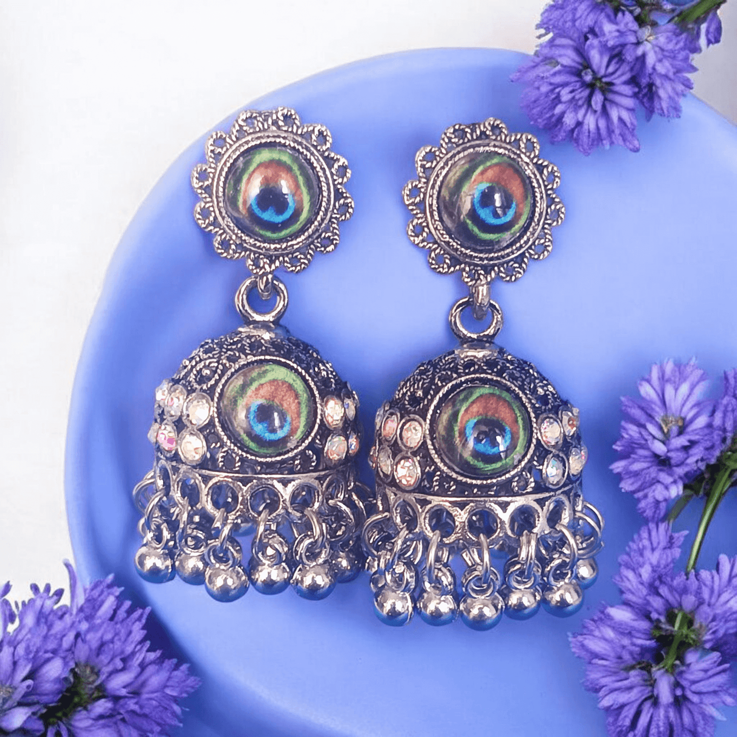 Peacock design oxidized silver jhumka earrings with rhinestones and lavender flowers background