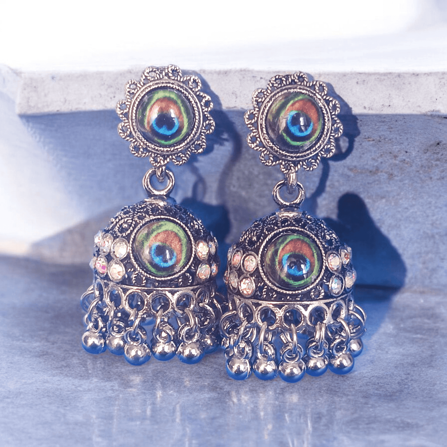 Peacock design oxidized silver jhumka earrings with rhinestones and concreate background