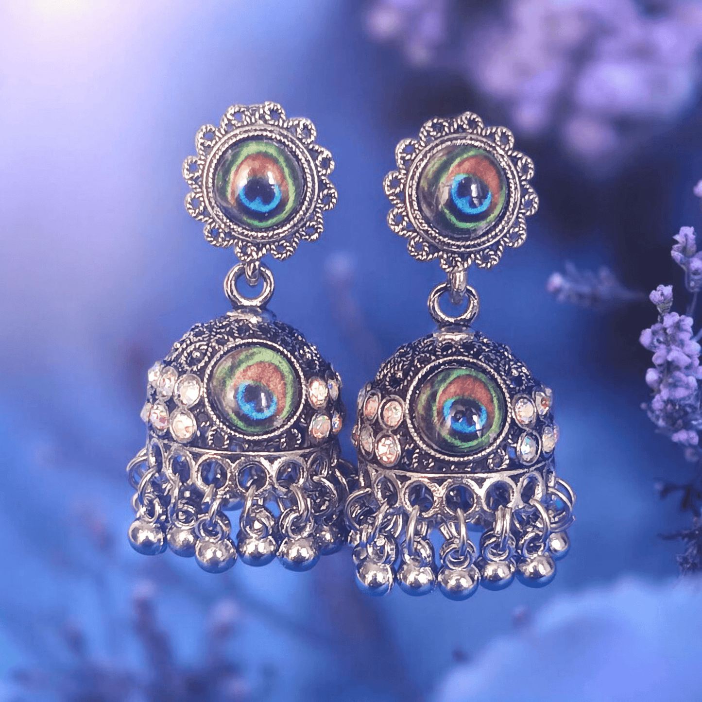 Peacock design oxidized silver jhumka earrings with rhinestones and lavender flowers background
