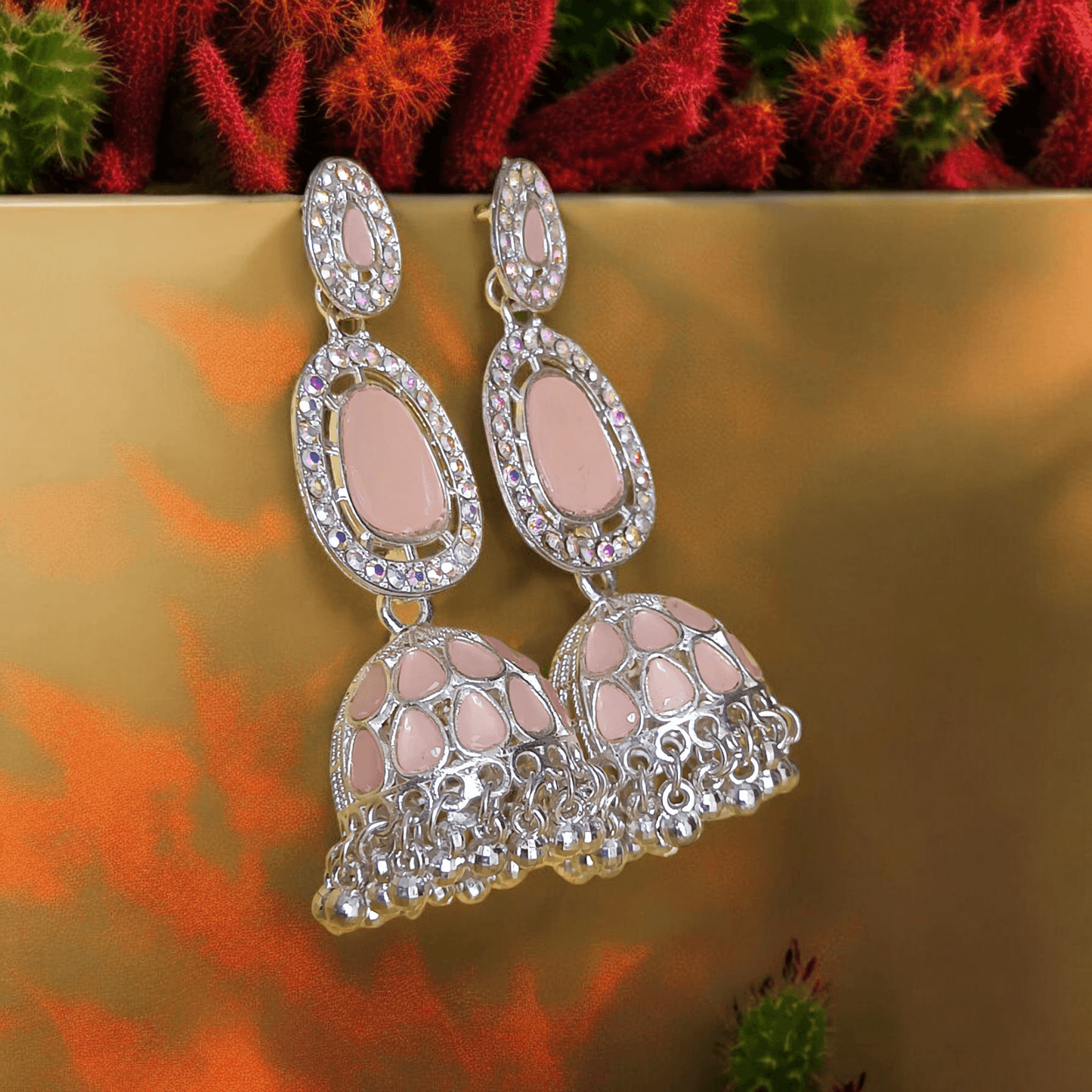 Selenesima peach oxidized jhumka earrings with embellishments against fabric and flower background