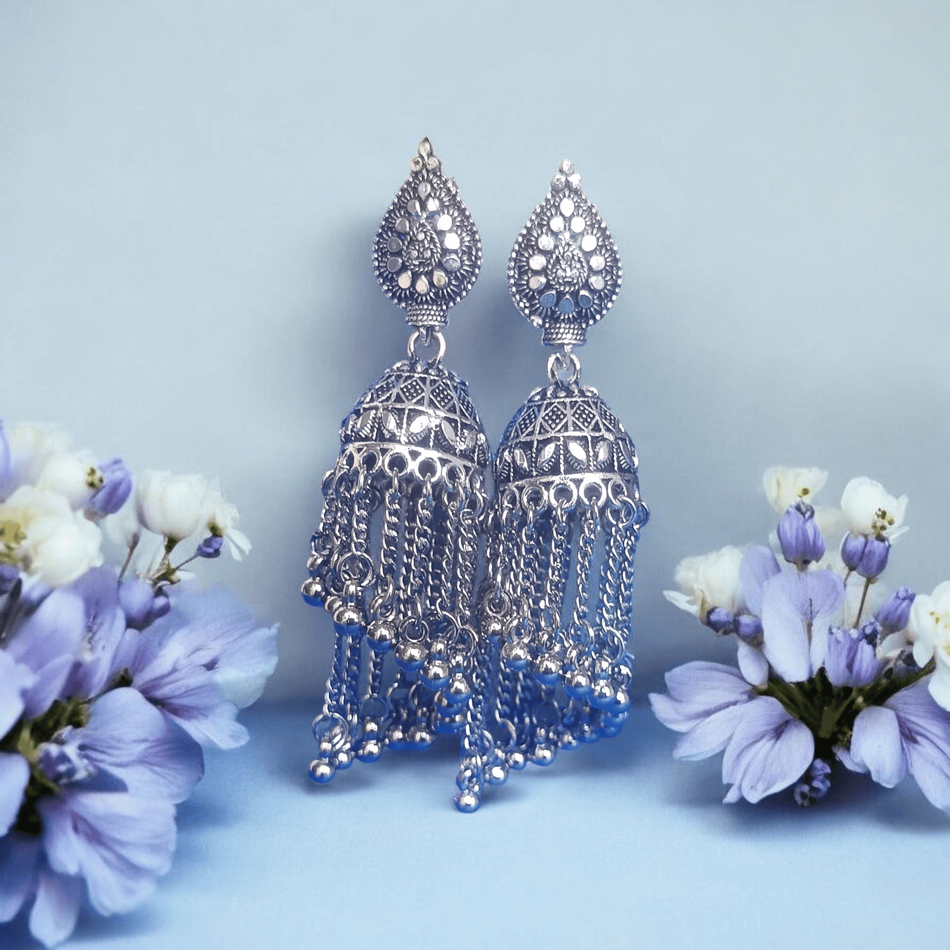 "Oxidized silver jhumka earrings with dome design and chain tassels on a Floral background – traditional Indian ethnic jewelry"