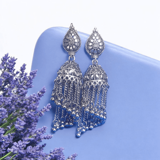 "Oxidized silver jhumka earrings with dome design and chain tassels on a lavender background – traditional Indian ethnic jewelry"
