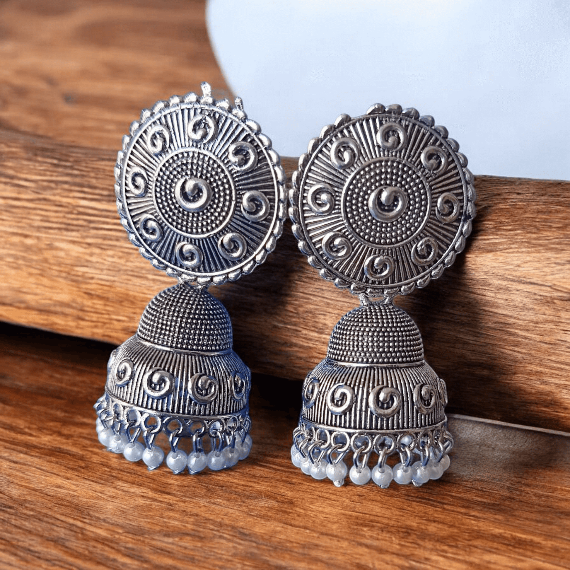 Handcrafted oxidized silver jhumka earrings with intricate designs and pearl drops against a wooden background