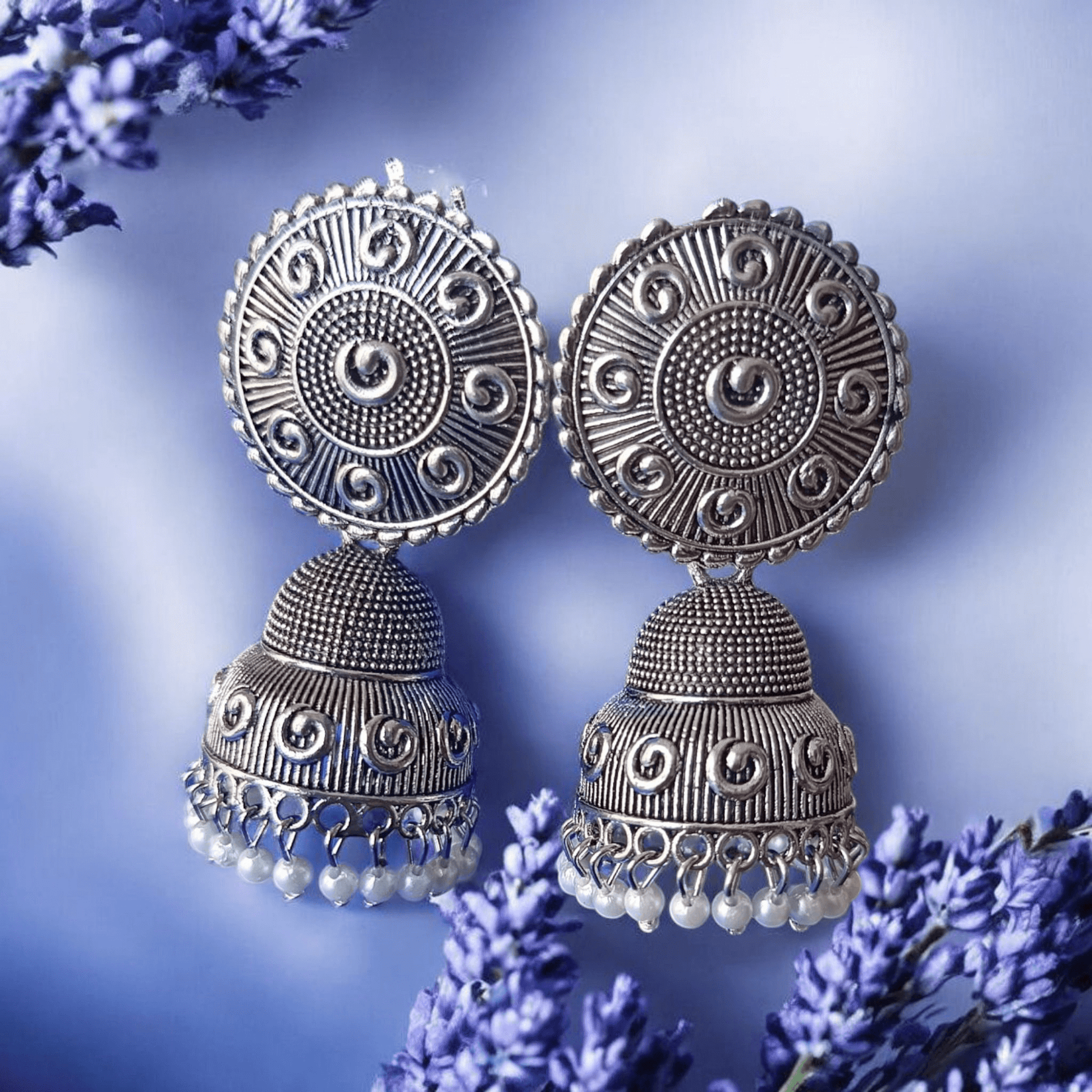 Handcrafted oxidized silver jhumka earrings with intricate designs and pearl drops against a lavender background