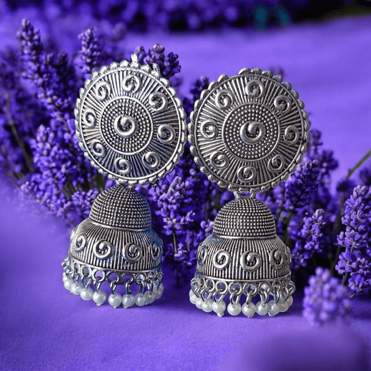 Handcrafted oxidized silver jhumka earrings with intricate designs and pearl drops against a lavender background