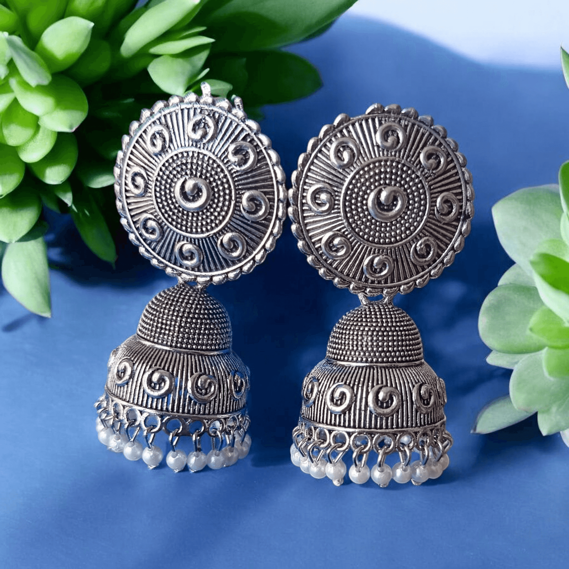 Handcrafted oxidized silver jhumka earrings with intricate designs and pearl drops against a lavender background