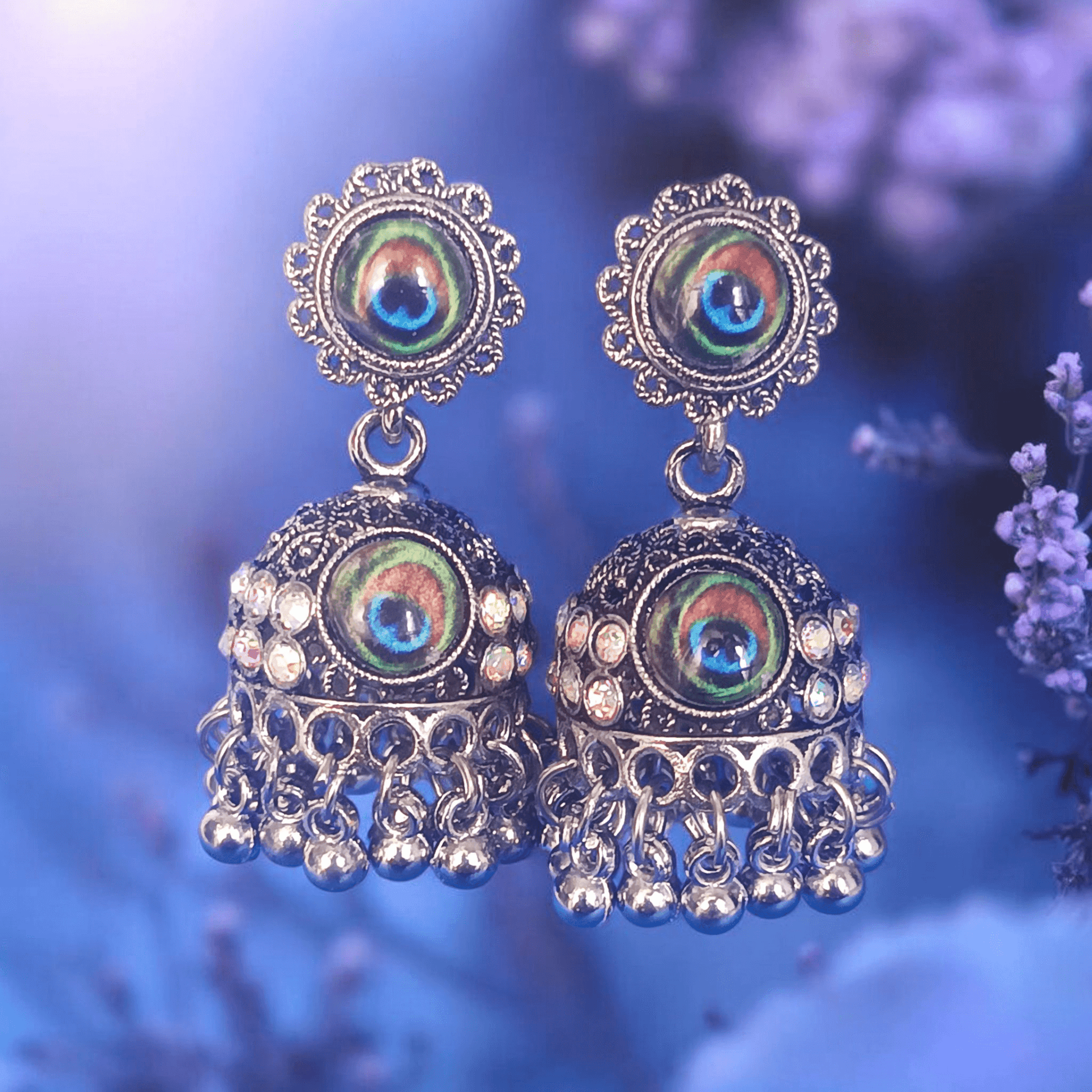 Peacock design oxidized silver jhumka earrings with rhinestones and lavender flowers background