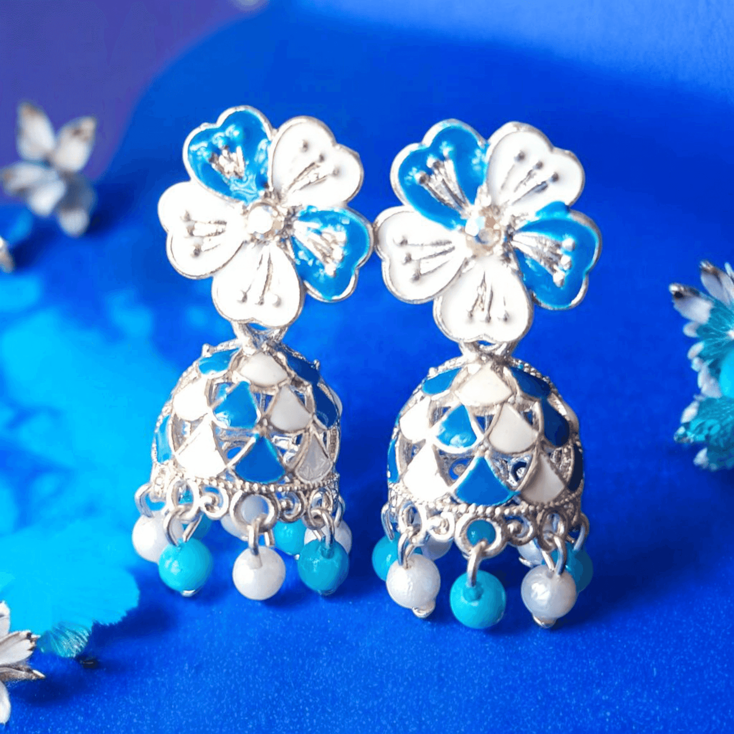 Selenesima blue floral oxidized jhumka earrings with pearls against blue background