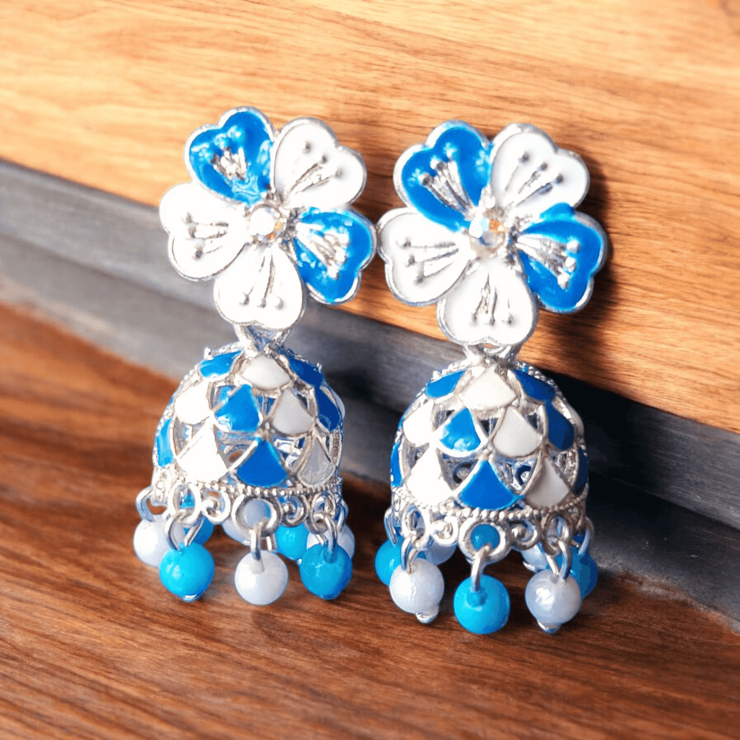 Selenesima blue floral oxidized jhumka earrings with pearls against wood background